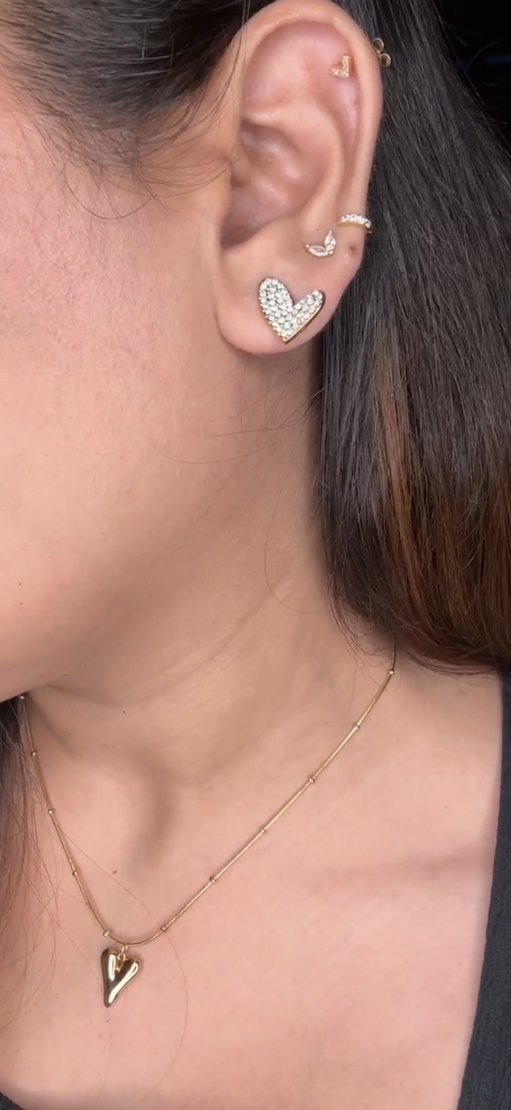 Close-up of an ear with heart-shaped earrings and a necklace.