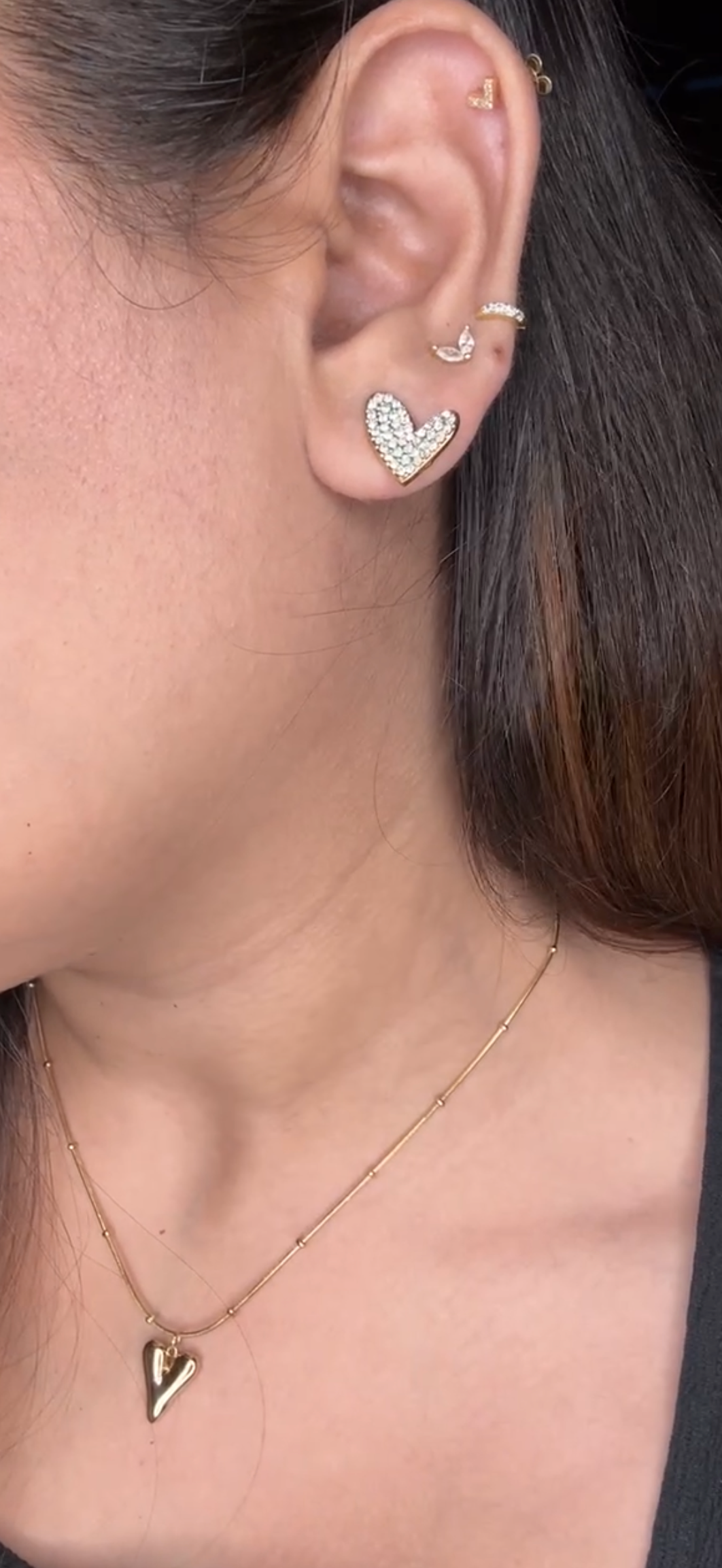 Close-up of an ear with heart-shaped earrings and a necklace.
